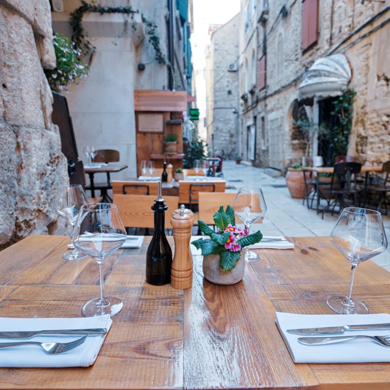 Outdoor restaurant summer terrace. Old vintage cafe with wooden table in europian old town.