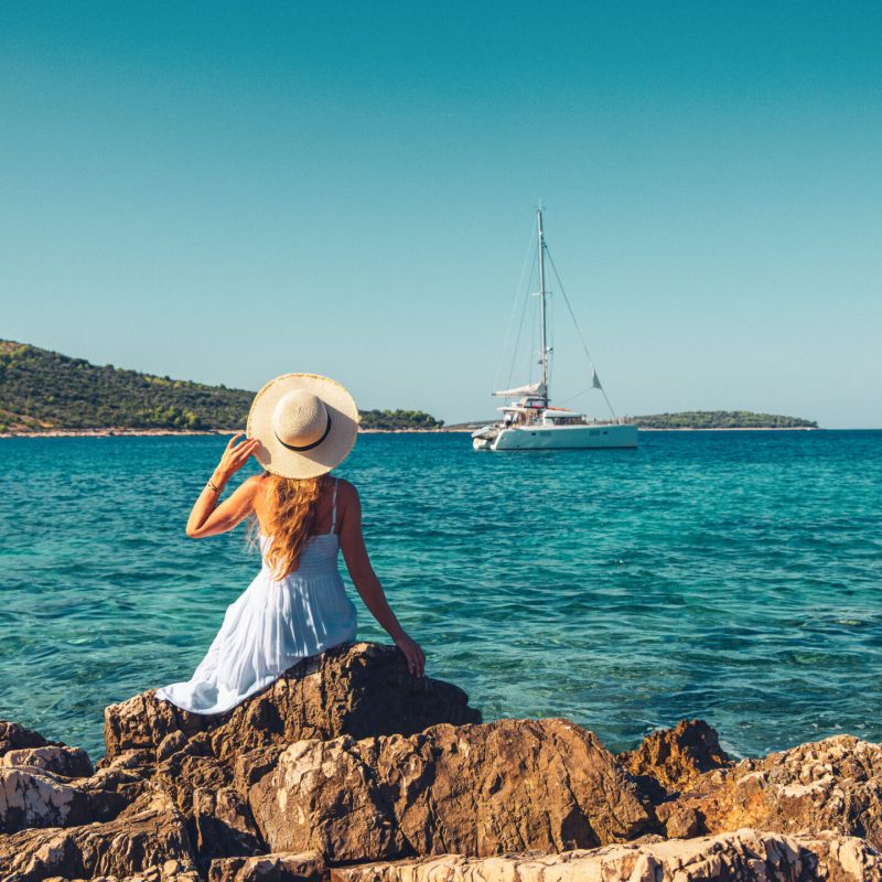 A girl with hat and white dress looking at yacht on the sea